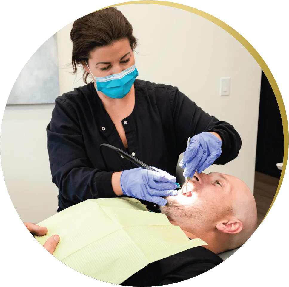 A dental hygienist wearing a mask and gloves provides preventive dental care to a patient lying in a chair
