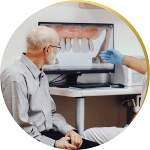 Elderly man consulting with a dentist about All on 4 Dental Implants, discussing treatment options displayed on a monitor.