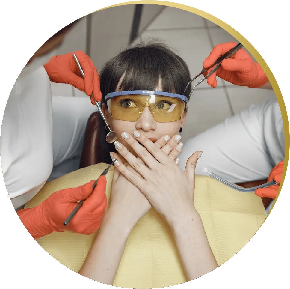 A patient with dark hair and yellow protective glasses is sitting in a dental chair, looking nervous. She covers her mouth with both hands while multiple gloved hands holding dental tools surround her for dental emergency in las vegas