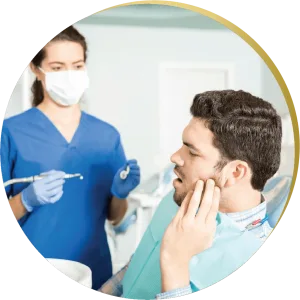 A male patient in a dental chair holding his cheek in pain, while a dentist in blue scrubs and a mask prepares to examine him for Reconstructive Dentistry Las Vegas