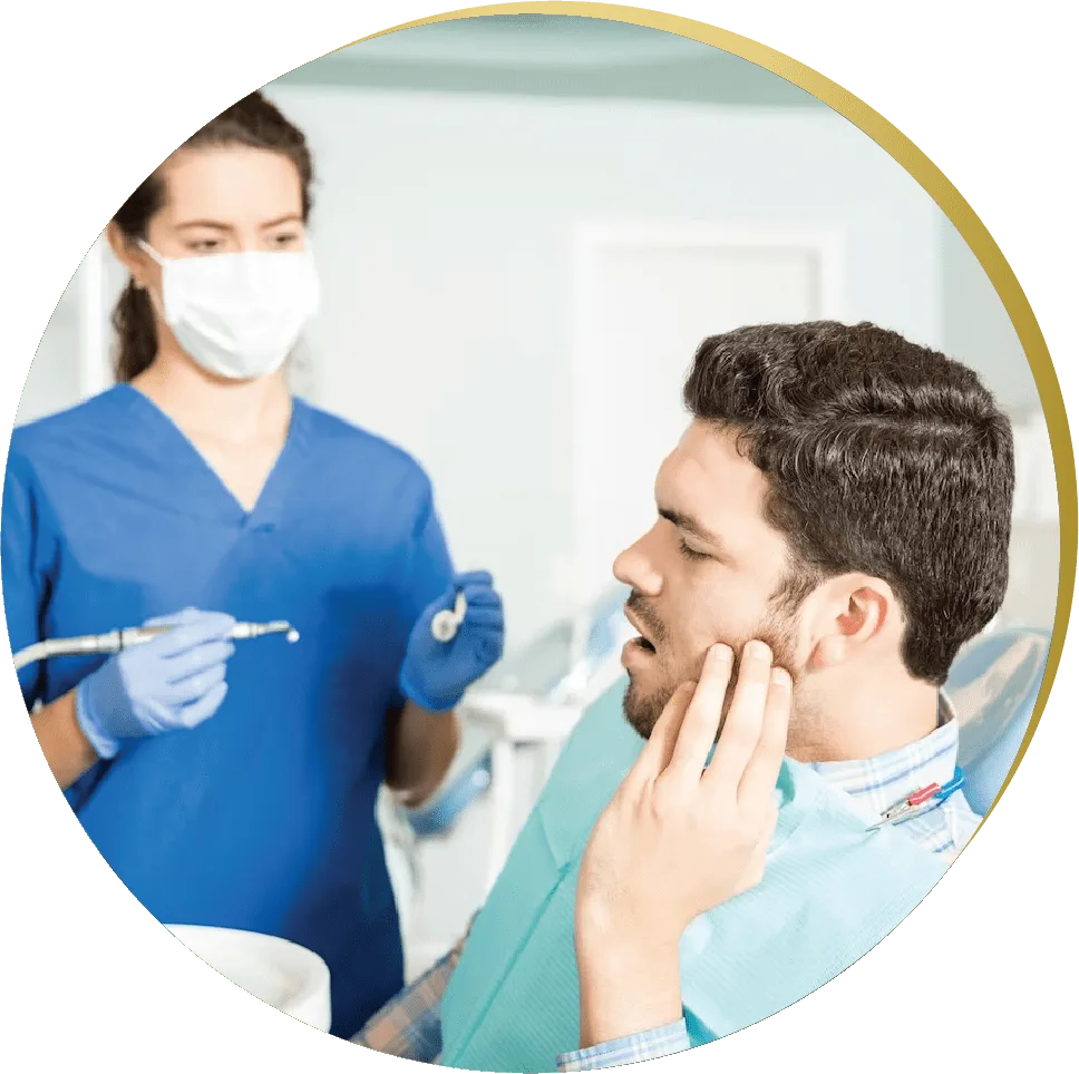 A male patient in a dental chair holding his cheek in pain, while a dentist in blue scrubs and a mask prepares to examine him for Reconstructive Dentistry Las Vegas
