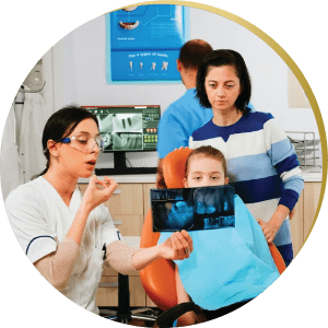 A female dentist shows a dental model to a young girl and her mother during a consultation in a family-friendly dental office. General and Family Dentistry.