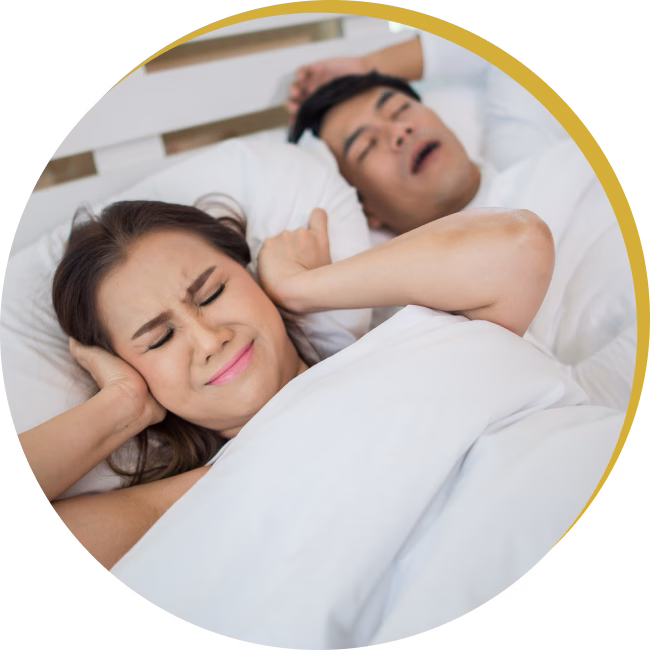 Wife covering her ears while husband snores loudly before starting sleep apnea treatment.